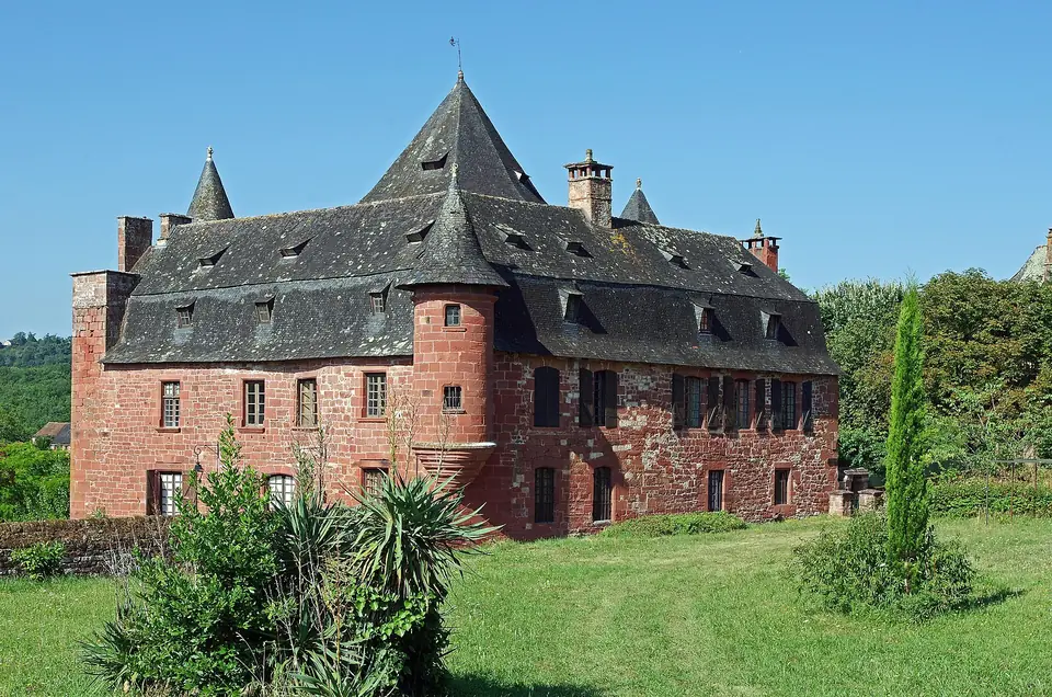 Castel de Vassinhac à Collonges-la-Rouge, manoir en grès rouge coiffé de toits d'ardoise, de tourelles et de lucarnes, entouré de verdure.