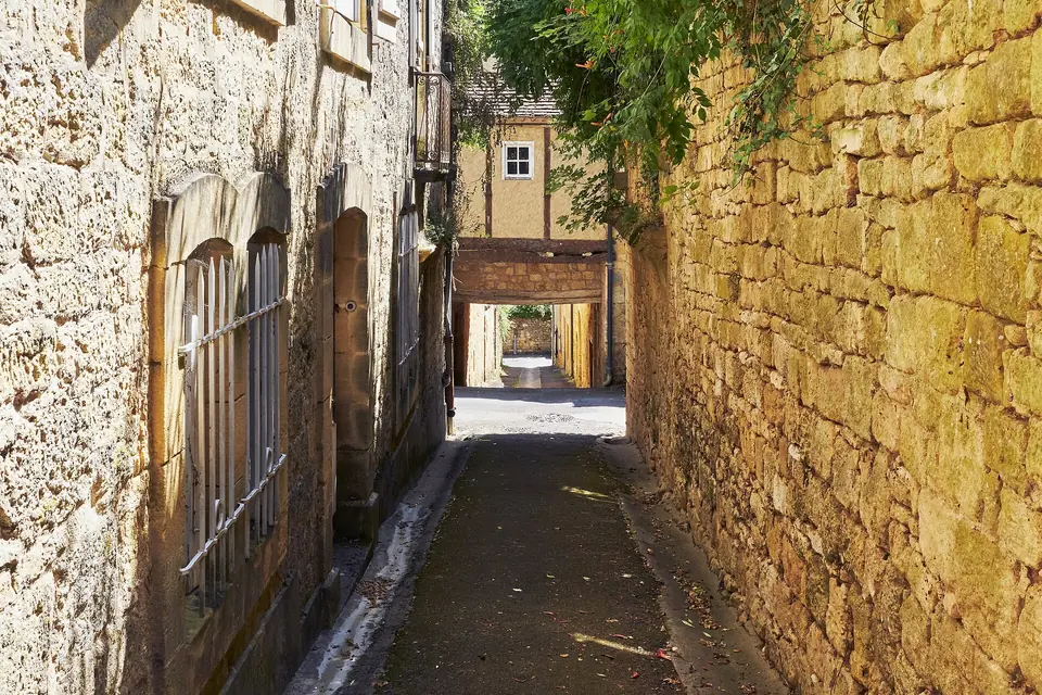 Ruelle étroite du village médiéval de Domme, bordée de murs en pierre dorée et de maisons aux fenêtres anciennes.
