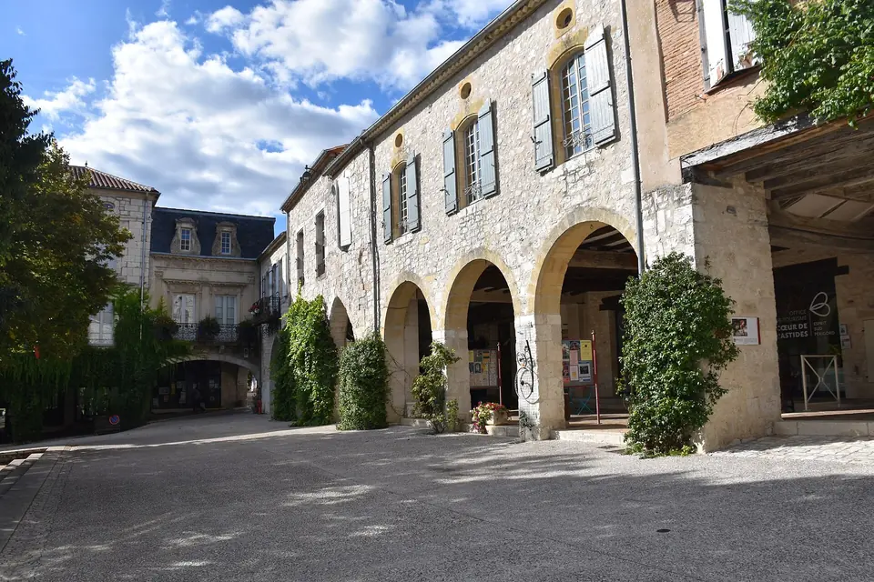 Arcades en pierre de la bastide de Monflanquin, maisons à étage aux fenêtres à volets et plantes grimpantes.