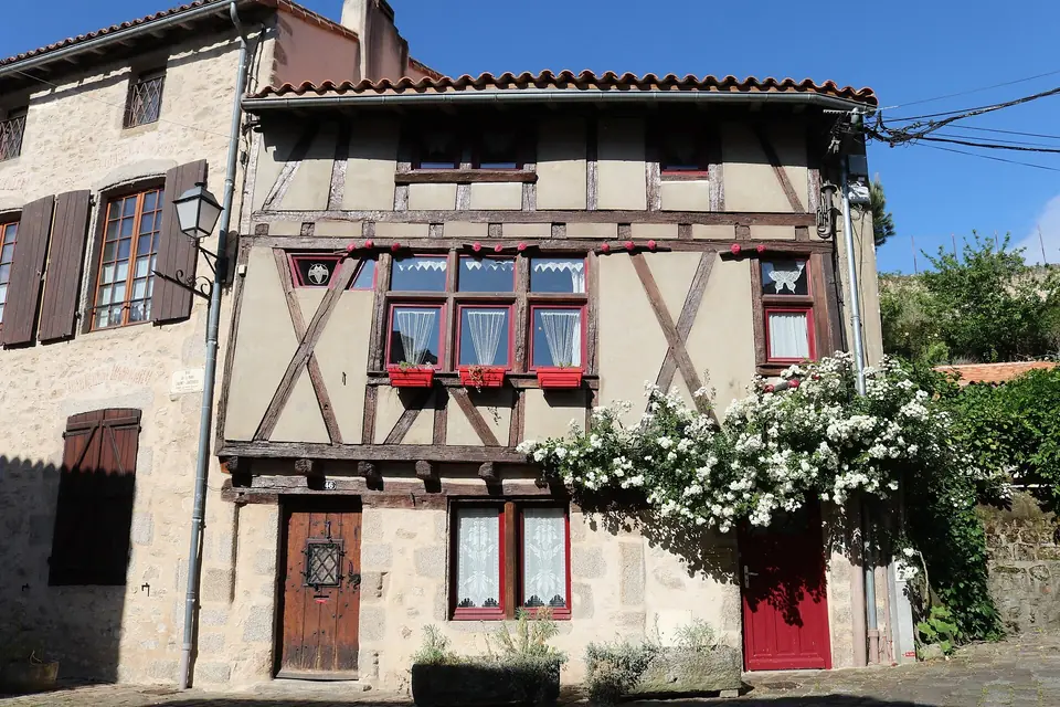 Maison à pans de bois rue de la Vau Saint-Jacques à Parthenay, avec fenêtres à volets, porte rouge et rosier grimpant en fleurs.