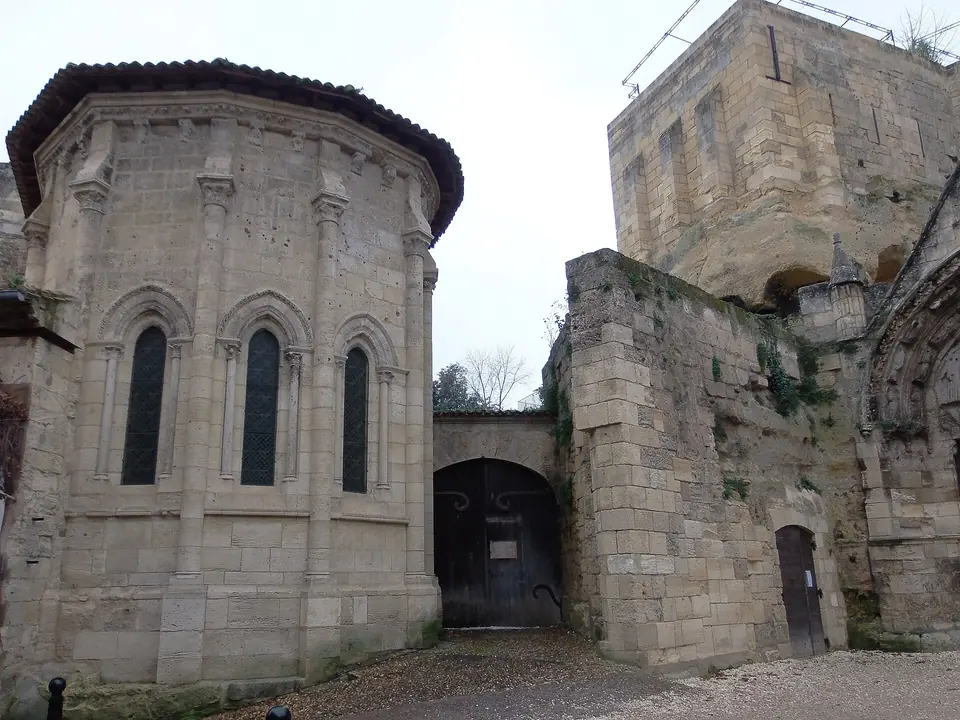 Chevet d'une chapelle romane et tour en pierre calcaire au cœur du village de Saint-Émilion, avec un passage voûté entre les murs.